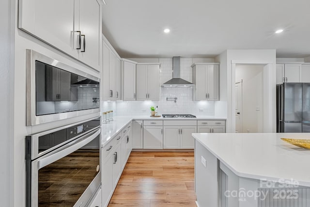 kitchen featuring stainless steel appliances, white cabinetry, wall chimney exhaust hood, and backsplash