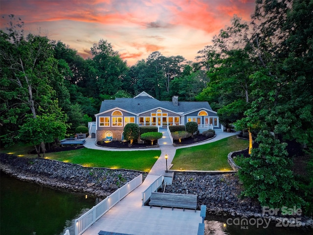 back house at dusk featuring a lawn