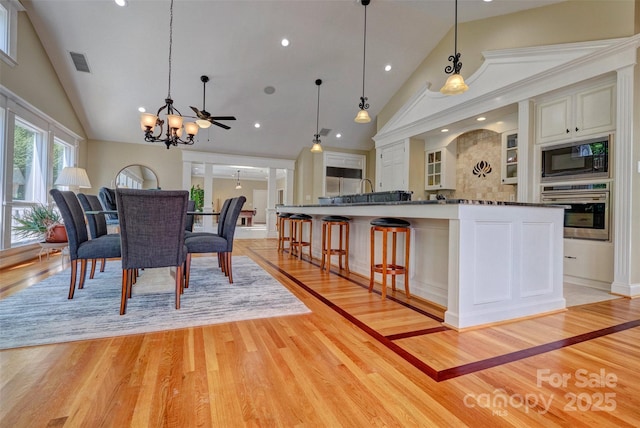 dining room with ceiling fan with notable chandelier, sink, high vaulted ceiling, and light hardwood / wood-style flooring