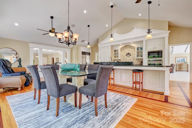 dining area featuring ceiling fan with notable chandelier, light hardwood / wood-style flooring, and vaulted ceiling