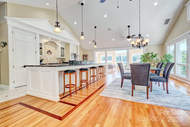 kitchen featuring hanging light fixtures, tasteful backsplash, a large island with sink, white cabinets, and ceiling fan with notable chandelier