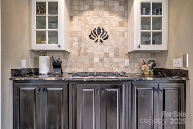 bar with tasteful backsplash, dark stone countertops, stainless steel gas stovetop, dark brown cabinets, and white cabinets