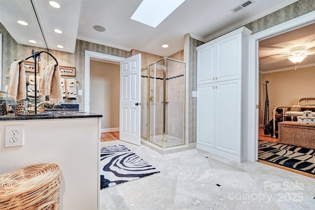 bathroom with a skylight, ornamental molding, vanity, ceiling fan, and a shower with shower door