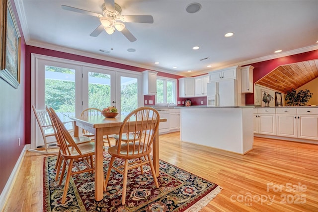 dining area with french doors, light wood-type flooring, crown molding, and a healthy amount of sunlight