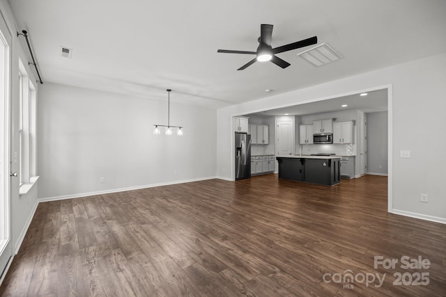 unfurnished living room featuring ceiling fan with notable chandelier and dark wood-type flooring