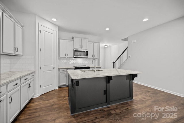 kitchen with a center island with sink, appliances with stainless steel finishes, sink, dark wood-type flooring, and light stone countertops