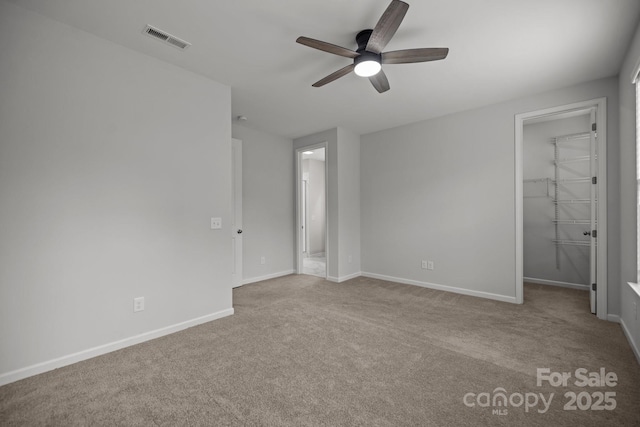 unfurnished bedroom with ceiling fan, a closet, light colored carpet, and a walk in closet