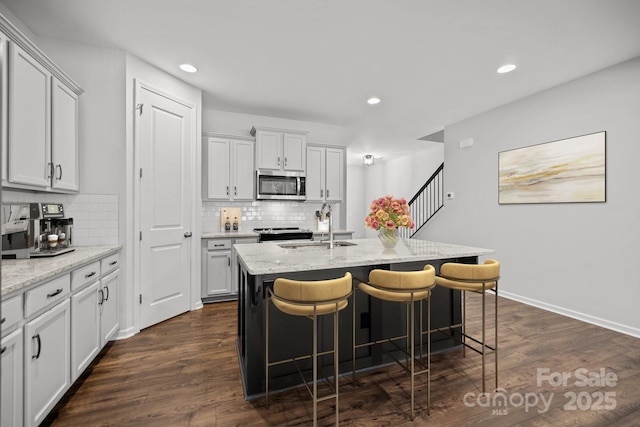 kitchen featuring a kitchen island with sink, stainless steel appliances, sink, light stone counters, and a kitchen breakfast bar