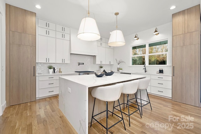 kitchen featuring a kitchen island, sink, pendant lighting, light hardwood / wood-style floors, and white cabinetry