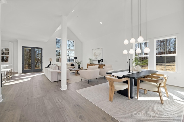 dining area with a healthy amount of sunlight, light hardwood / wood-style flooring, high vaulted ceiling, and french doors