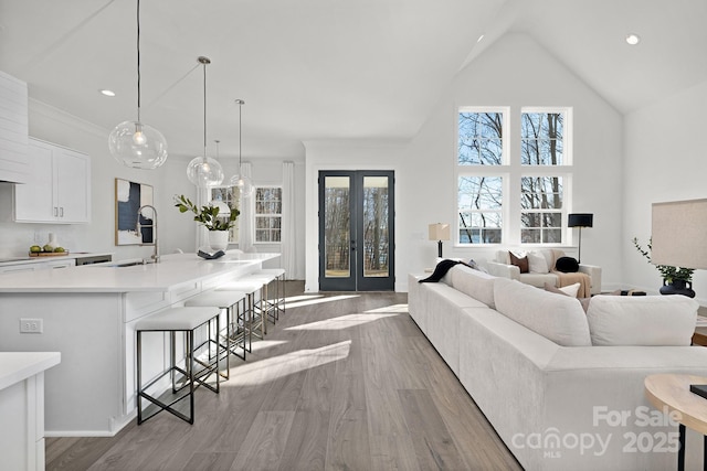 living room with lofted ceiling, french doors, sink, and light hardwood / wood-style flooring