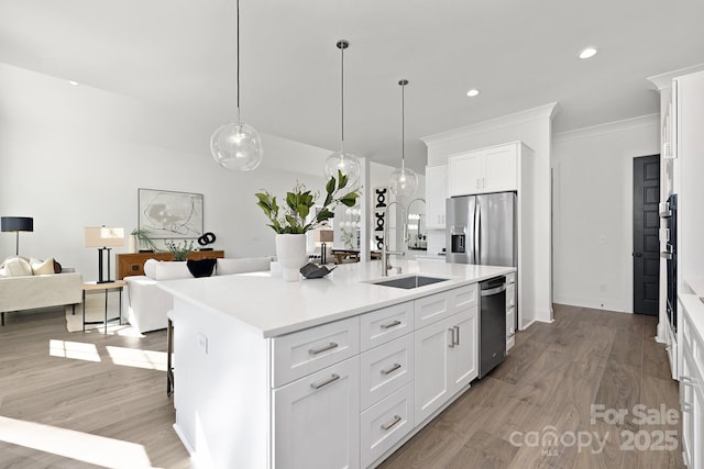 kitchen featuring sink, crown molding, decorative light fixtures, a center island with sink, and white cabinets