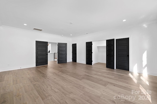 unfurnished bedroom featuring ornamental molding, two closets, and light wood-type flooring