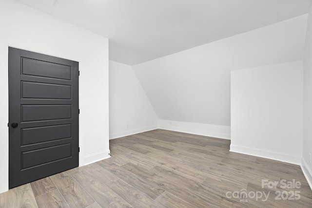 additional living space with vaulted ceiling and light hardwood / wood-style flooring