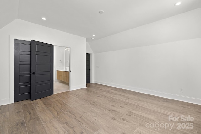 interior space featuring light wood-type flooring, vaulted ceiling, and connected bathroom