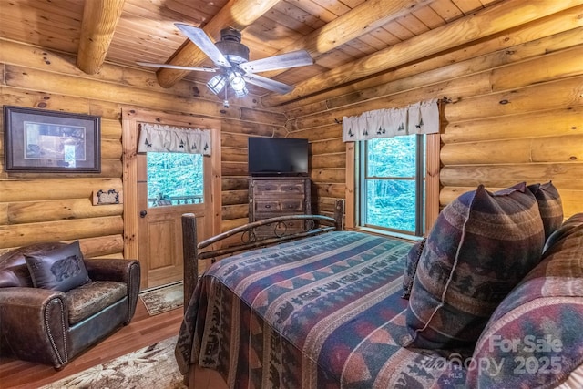 bedroom with beamed ceiling, wood-type flooring, rustic walls, and ceiling fan