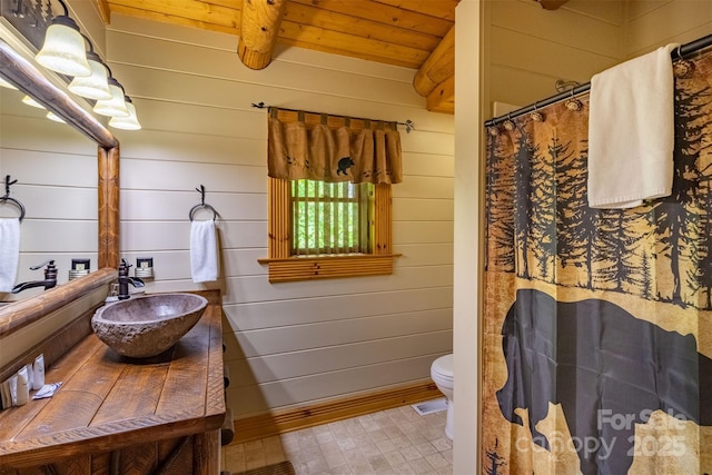 bathroom featuring beam ceiling, wooden ceiling, toilet, wooden walls, and vanity