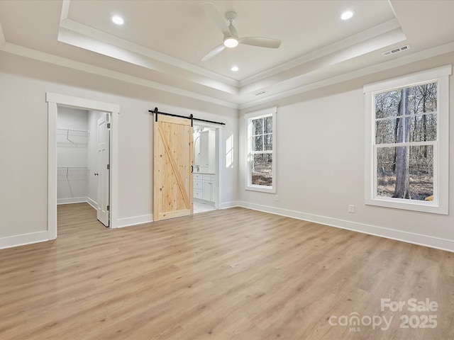 unfurnished bedroom featuring a spacious closet, ensuite bath, a raised ceiling, ceiling fan, and a barn door