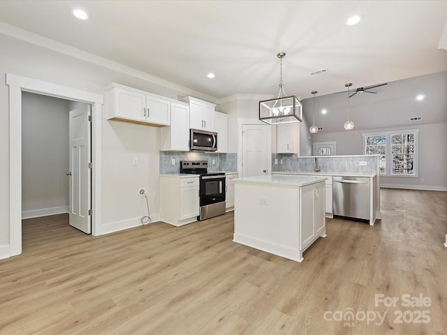 kitchen with appliances with stainless steel finishes, decorative backsplash, hanging light fixtures, a kitchen island, and white cabinets