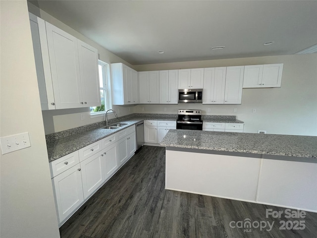 kitchen with dark wood-type flooring, dark stone counters, white cabinets, sink, and stainless steel appliances