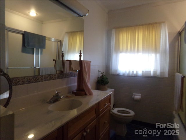 bathroom with an enclosed shower, vanity, crown molding, tile walls, and toilet