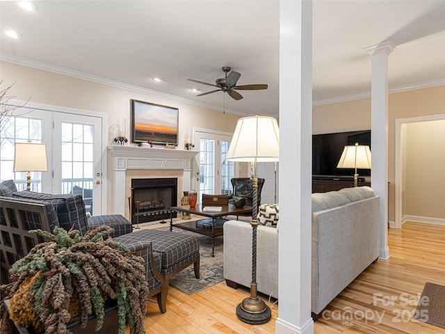 living room with ornate columns, ceiling fan, light hardwood / wood-style flooring, crown molding, and a tiled fireplace