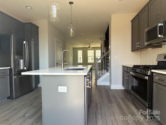 kitchen featuring backsplash, a center island with sink, sink, hardwood / wood-style flooring, and appliances with stainless steel finishes