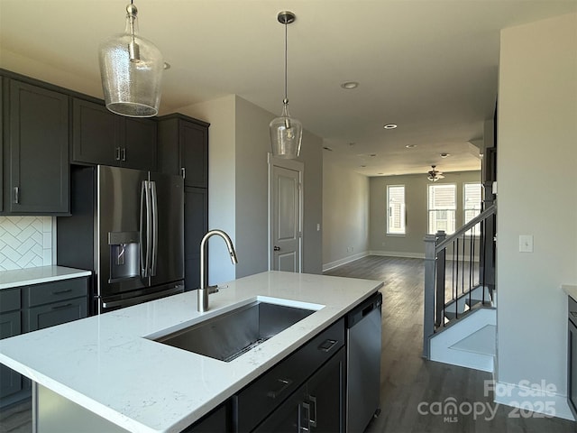 kitchen with a center island with sink, sink, decorative backsplash, light stone countertops, and appliances with stainless steel finishes