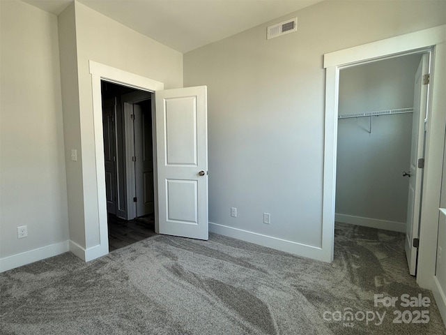 unfurnished bedroom with a walk in closet, dark carpet, and a closet