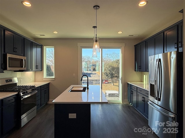 kitchen with pendant lighting, dark wood-type flooring, sink, an island with sink, and stainless steel appliances