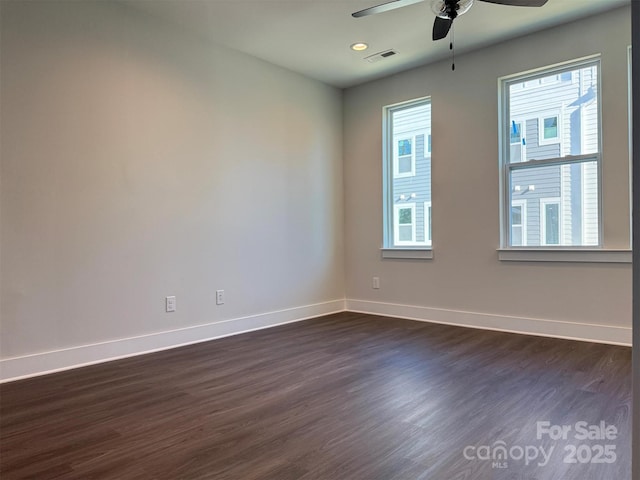 spare room featuring visible vents, plenty of natural light, dark wood-type flooring, and baseboards