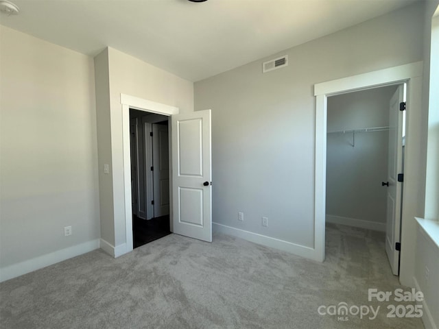 unfurnished bedroom featuring visible vents, a walk in closet, baseboards, carpet flooring, and a closet