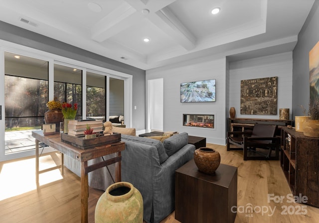 living room featuring coffered ceiling, beam ceiling, a large fireplace, and light wood-type flooring