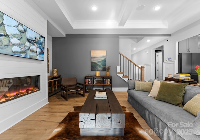 living room with beamed ceiling, wood-type flooring, crown molding, and a fireplace