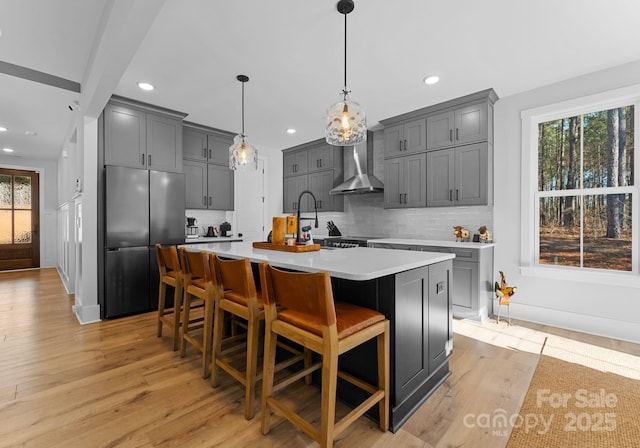 kitchen with decorative light fixtures, stainless steel fridge, a kitchen breakfast bar, a kitchen island with sink, and decorative backsplash