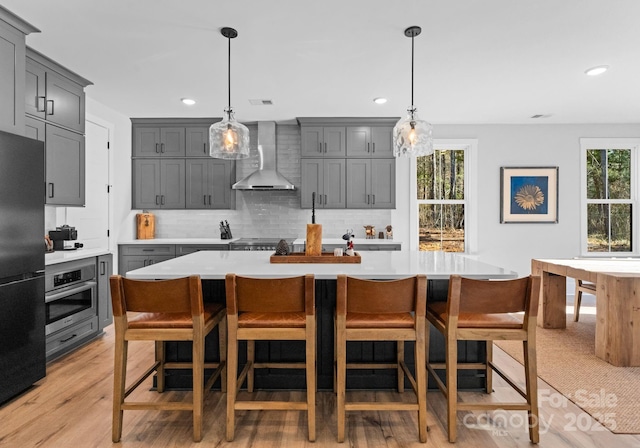 kitchen featuring a spacious island, gray cabinetry, oven, and wall chimney exhaust hood