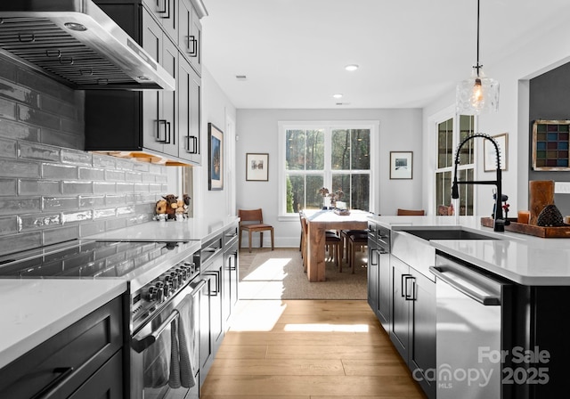 kitchen with wall chimney exhaust hood, sink, decorative light fixtures, appliances with stainless steel finishes, and backsplash