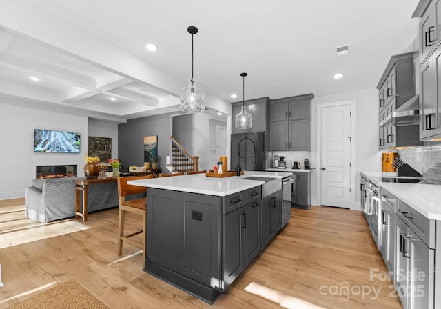 kitchen featuring coffered ceiling, beamed ceiling, an island with sink, pendant lighting, and backsplash