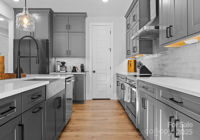 kitchen with decorative light fixtures, light hardwood / wood-style flooring, gray cabinets, stainless steel appliances, and wall chimney range hood