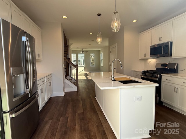 kitchen with ceiling fan, sink, hanging light fixtures, stainless steel appliances, and a center island with sink