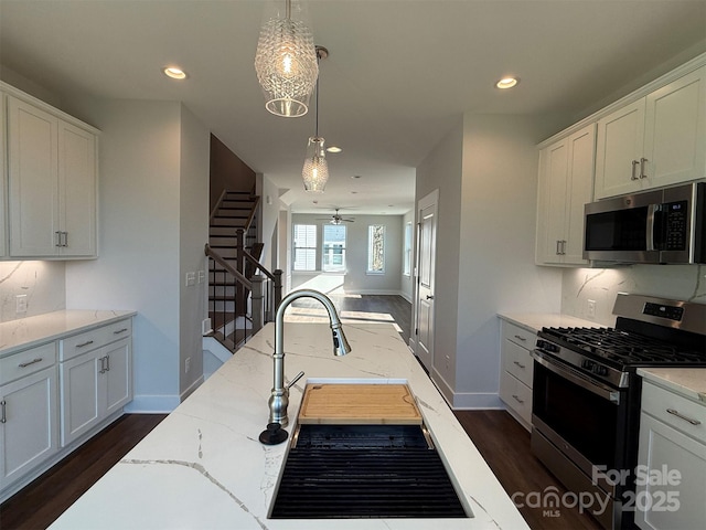 kitchen with light stone countertops, appliances with stainless steel finishes, ceiling fan, pendant lighting, and white cabinetry