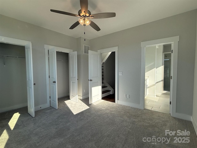 unfurnished bedroom featuring two closets, dark carpet, and ceiling fan