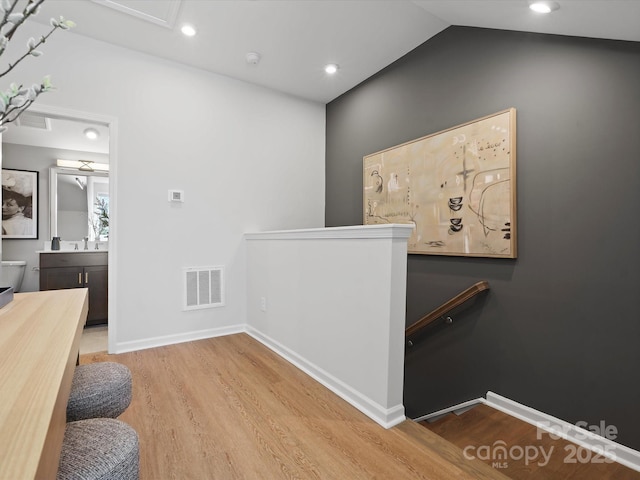 corridor with visible vents, wood finished floors, an upstairs landing, and baseboards