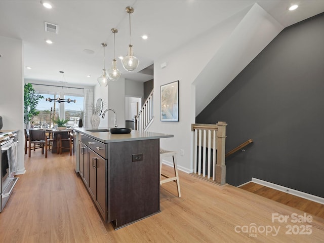 kitchen with light wood-type flooring, dark brown cabinets, a kitchen bar, and a sink