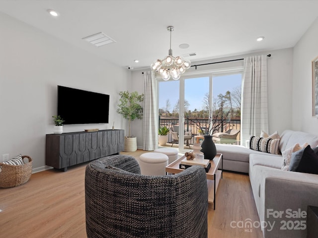 living room featuring baseboards, visible vents, light wood finished floors, and an inviting chandelier