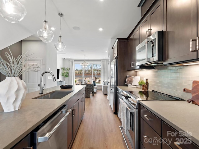 kitchen featuring light wood finished floors, decorative backsplash, stainless steel appliances, dark brown cabinets, and a sink