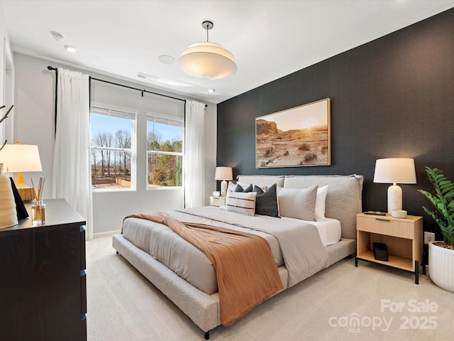 bedroom with an accent wall, light carpet, visible vents, and baseboards