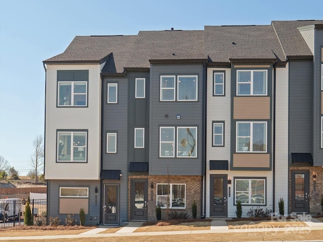 townhome / multi-family property with roof with shingles, fence, and brick siding