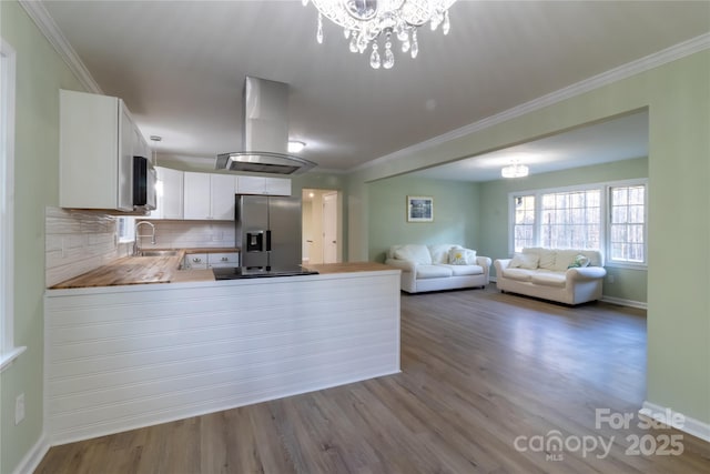 kitchen with kitchen peninsula, stainless steel fridge, island range hood, a notable chandelier, and white cabinetry