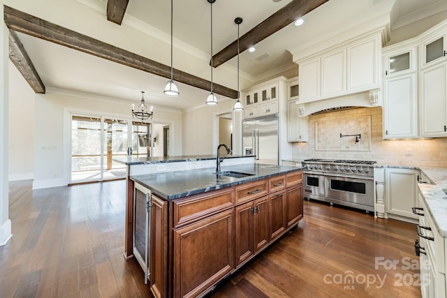 kitchen with sink, a kitchen island with sink, backsplash, high quality appliances, and white cabinets